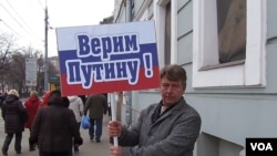 俄罗斯吞并克里米亚后,当局去年3月在莫斯科组织亲政府支持普京集会游行。普京的一名支持者手举标语:我们信任普京。(美国之音白桦拍摄)