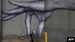 一位女士戴着口罩走过纽约市中城一座大楼的巨手壁画。(2020年4月22日)