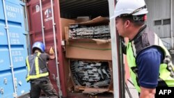 Sejumlah petugas membuka peti kemas berisi limbah elektronik yang disita di Port Klang di pinggiran Kota Kuala Lumpur, 26 Juni 2024. (Foto: AFP)