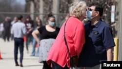 资料照片:在新冠疫情下举行的总统初选期间,选民杰夫·特拉吉茨(右)和罗丽·沃尔特在威斯康星州密尔沃基市的一处投票站外排队等候投票时戴着口罩亲吻。(2020年4月7日)