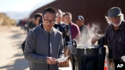 资料照片:一名来自中国的男子在加利福尼亚州贾库姆巴附近越过美墨边境进入美国后,一边吃着一碗麦片,一边等待申请庇护。(2023年10月24日)