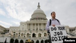 Một công chức chính phủ liên bang, đứng trên thềm trụ sở Quốc hội, cầm tấm bảng với dòng chữ "Xin hãy thực hiện phần việc của quý vị để tôi có thể làm công việc của tôi"