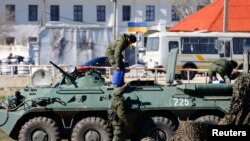 据信是俄罗斯军人的武装人员在港口城市费奥多西亚的乌克兰海军陆战队基地外向辆装甲运兵车上输送给养物资。(2014年3月23日)