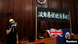 一名进入香港立法会的抗议者站在挂在立法会内的港英旗帜旁使用扩音喇叭讲话。(2019年7月1日)