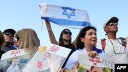 2025 年 2 月 1 日,人们在特拉维夫人质广场的屏幕上观看释放加沙地带的以色列人质时,他们举着刚刚获释的以色列人质亚登·比巴斯 (Yarden Bibas) 及其两个孩子科菲尔 (Kfir) 和阿里尔 (Ariel) 的照片。