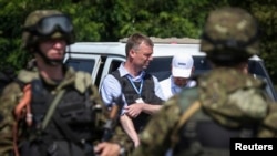 2014年7月30日，驻乌克兰的欧安组织监督使命团的亚历山大•哈格，站在手持武器的亲俄分离分子身边，此时欧安组织车队正在前往马航班机坠机现场。