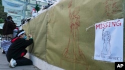 资料图片:2021年12月24日(星期五),香港大学拆除纪念八九民运的“民主女神”雕像后,一名大学生在现场写下笔记。(美联社)