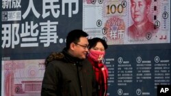 一对青年男女走过北京街头宣传中国新版人民币100元钞票的广告牌。(2016年1月11日)