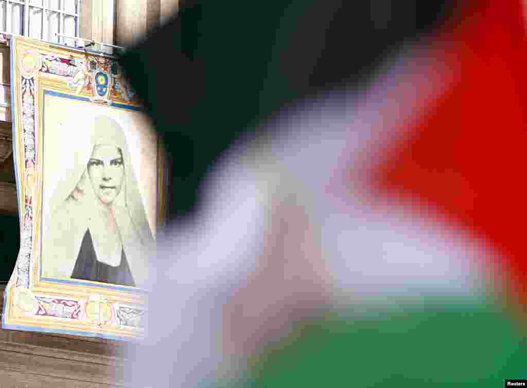 A Palestinian flag waves in front of a tapestry of Mariam Baouardy Haddad before Pope Francis leads a ceremony for the canonization of four nuns at Saint Peter's square in the Vatican City, May 17, 2015.