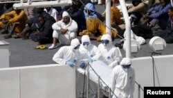 Những di dân sống sót ngồi trên tàu tuần duyên Bruno Gregoretti của Ý trong lúc thi thể người thiệt mạng được khiêng ra khỏi tàu tuần duyên Bruno Gregoretti của Ý tại Senglea, Valletta Grand Harbour, ngày 20 tháng 4, 2015.