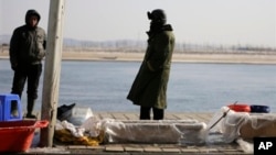 中国渔民在丹东的河边卖鱼,河对岸是朝鲜边境城镇新义州。(2013年2月7日)