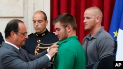 法国总统奥朗德把法国荣誉军团勋章别在美国国民警卫队成员阿列克·斯卡拉托斯身上,美国空军士兵斯宾塞·斯通在旁观看。(2015年8月24日)