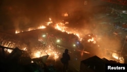 在与警察的对峙中一名抗议者在香港理工大学的校园里站在燃烧的大火旁。(2019年11月18日)