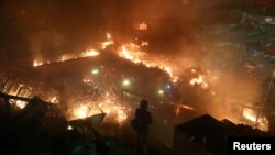 在与警察的对峙中一名抗议者在香港理工大学的校园里站在燃烧的大火旁。(2019年11月18日)