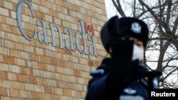 在加拿大驻北京大使馆外一名中国警察向摄影记者打手势。(2018年12月12日)