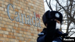 在加拿大驻北京大使馆外一名中国警察向摄影记者打手势。(2018年12月12日)