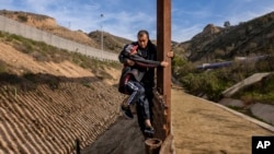 一位洪都拉斯人带儿子在加利福尼亚州美墨边界从墨西哥一侧翻越围墙(2018年12月22日)