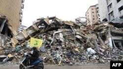 以色列和真主党之间的停火生效后,人们陆续返回家园,一名男子经过贝鲁特南郊一栋建筑的废墟时挥舞着真主党的旗帜。(法新社:2024年11月27日)