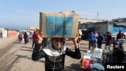 资料照片:在加沙中部的代尔巴拉赫地区,一名巴勒斯坦人头顶联合国近东巴勒斯坦难民救济和工程处(UNRWA)分发的援助物品箱。(2024年11月4日)