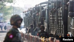 FILE- Soldiers stand next to military vehicles as people gather to protest against the military coup, in Yangon, Myanmar, Feb. 15, 2021.