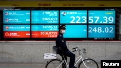 一名戴着口罩的日本警察骑车停站在东京街头一个日经指数电子显示板前。(路透社2020年2月26日资料照)