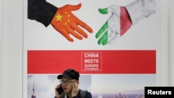 2019 年 5 月 28 日,在中国北京举行的中国国际服务贸易博览会上,一名男子在一张写着“中国在佛罗伦萨遇见欧洲”的海报旁边接听电话。