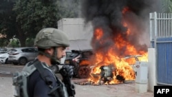 在以色列南部城市斯德罗特,一名以色列保安部队士兵站在一辆被哈马斯发射的导弹击中的汽车旁。(2023年10月9日)