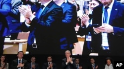 历经协议难产而延会,COP29主席穆赫塔尔·巴巴耶夫(中)在闭幕全体会议上率众鼓掌。(美联社:2024年11月24日)