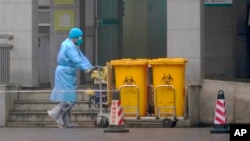 身穿防护服的工人推着医疗垃圾桶走过武汉医疗中心大门。(2020年1月22日)