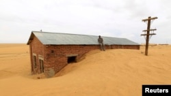 A worker rests on the roof of a building surrounded by sand as a result of desert encroachment at Ogrein Railway Station at the Red Sea State August 1, 2013.