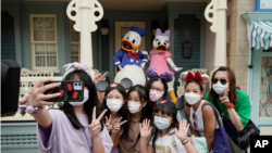 在香港迪士尼乐园,戴着口罩的游客与标志性卡通人物唐老鸭和黛丝鸭自拍。(2020年9月25日)