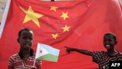 在中国资助的有千所住房单位的吉布提建筑工程启动仪式之前,拿着吉布提国旗的小男孩站在巨大的中国国旗前。(2018年7月4日)