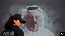 资料照片:在人们在沙特驻伊斯坦布尔领事馆附近举行周年纪念仪式之前,一名土耳其警察走过遇害记者卡舒吉的画像。(2019年10月2日)