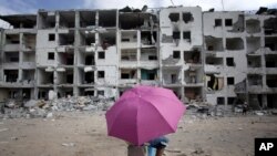 一名巴勒斯坦男孩打着伞在加沙地带北部的一处遭到破坏的居民区休息(2014年8月11日)