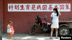 资料照:一个妈妈和孩子在“计划生育是我国基本国策”的标语前走过。(2002年7月23日)