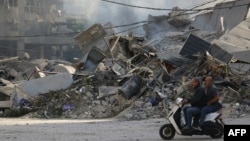 两名男子骑着摩托车驶过夜间以色列空袭贝鲁特南部郊区被炸毁的一处目标。(2024年10月3日)