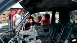 在巴格达萨德尔城一处热闹的露天旧家具市场外的爆炸现场,男孩查看一辆被炸毁汽车。(2021年4月15日)