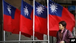 资料照:一名妇女走过台北街道旁飘扬的台湾旗帜。