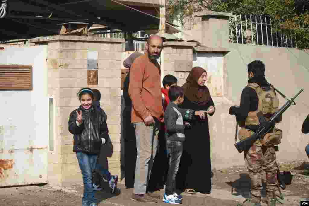 2017年1月23日,六岁的阿娅打着胜利的手势,她的家人与伊拉克军人交谈,报告他们了解的有关“伊斯兰国”激进分子的信息。(美国之音希瑟·默多克拍摄)  