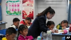 资料图片:2023年9月5日,在媒体组织的四川省甘孜州稻城县的参观活动中,香格里拉镇重点寄宿制学校一年级的一名老师在帮助一名学生写字母。(美联社)