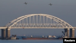 俄罗斯截停乌克兰船只后,俄罗斯喷气式战斗机飞过一座连接俄罗斯大陆与克里米亚半岛的桥梁,桥下面有一艘货船。
