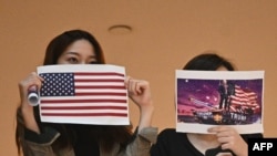 两名香港女子在一个商场内举行的抗议中国人大制定港版国安法的集会上手举美国国旗和川普总统画像。(法新社2020年5月28日)