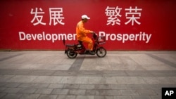 2015年7月15日北京市中心的一条街道上,一名维修工人骑着摩托车经过用中英文写着“发展”和“繁荣”的横幅