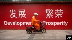 资料照:一名男子骑车路过北京市中心一堵宣传墙。(2015年7月15日)