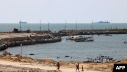 2024年5月7日,巴勒斯坦人走过加沙城的一个码头,这里是美国中央司令部宣布的人道主义“海上走廊”的一部分,可以看到海岸附近的海军舰船。(法新社照片)