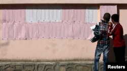 Afghan boys look on a preliminary list taped to the wall of a polling station in Kabul, April 7, 2014.