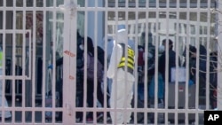 身穿防护服的工作人员看着从海外抵达北京的旅客进入北京国际会展中心等待接受进一步的健康甄别。(2020年3月18日)