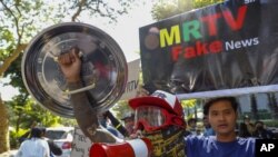 示威者在2021年2月11日星期四对缅甸曼德勒举行的军事政变抗议游行中,展示了谴责国家和军事电视台的标语牌。