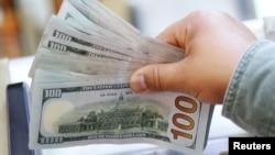 资料照：一人手拿一叠百元美钞。