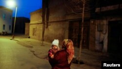 资料照:中国新疆喀什一名维吾尔族妇女抱着一个孩子。(2017年3月23日)